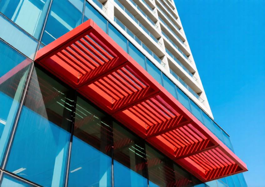 Close-up of red powder-coated aluminum sun louvers casting shadows on glass façade