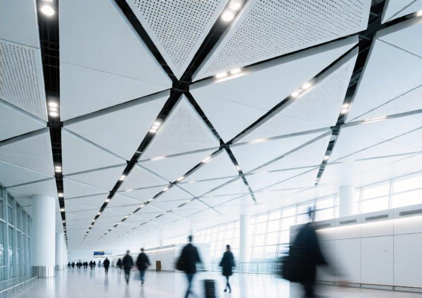 Perforated matte white aluminum ceiling panels in a modern airport terminal.